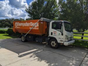 Dumpster Dogs truck delivering an orange roll-off dumpster to a Tampa Bay home